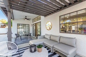 A covered outdoor seating area with a sofa, a round table, and a chair. - Modern-Terranean Escape | Pool & Spa | 2 Primary's (Scottsdale)
