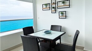 Ein Balkon mit einem Glastisch und Korbstühlen, mit Blick auf das blaue Meer.