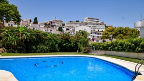 Piscina com água azul cristalina, rodeada por vegetação e edifícios ao fundo.