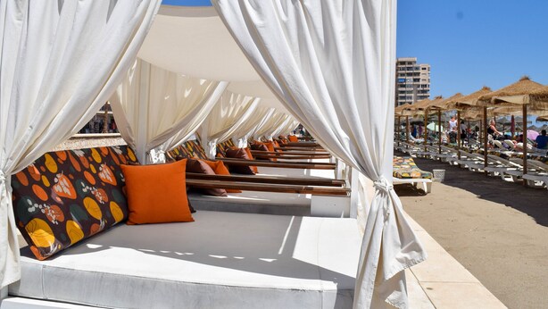 Uma cabana de praia com toldo, assentos acolchoados e almofada estampada.