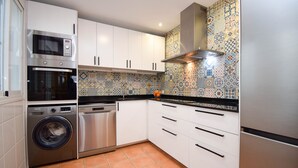 Uma cozinha com armários brancos, máquina de lavar, lava-louças, micro-ondas e painel de azulejos.