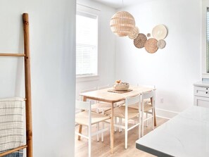 A bright, minimalist dining area with a wooden table and white chairs, a woven pendant light, and a wall-mounted decorative piece. - Private, updated 30a Beach Bungalow (Santa Rosa Beach)