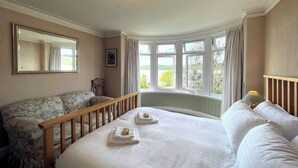 Ein Schlafzimmer mit einem Bett, einem Holckrippenbett, einem Fenster mit Vorhängen und einem Spiegel an der Wand.