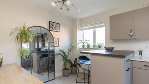 A modern kitchen with a central island, bar stools, and potted plants.