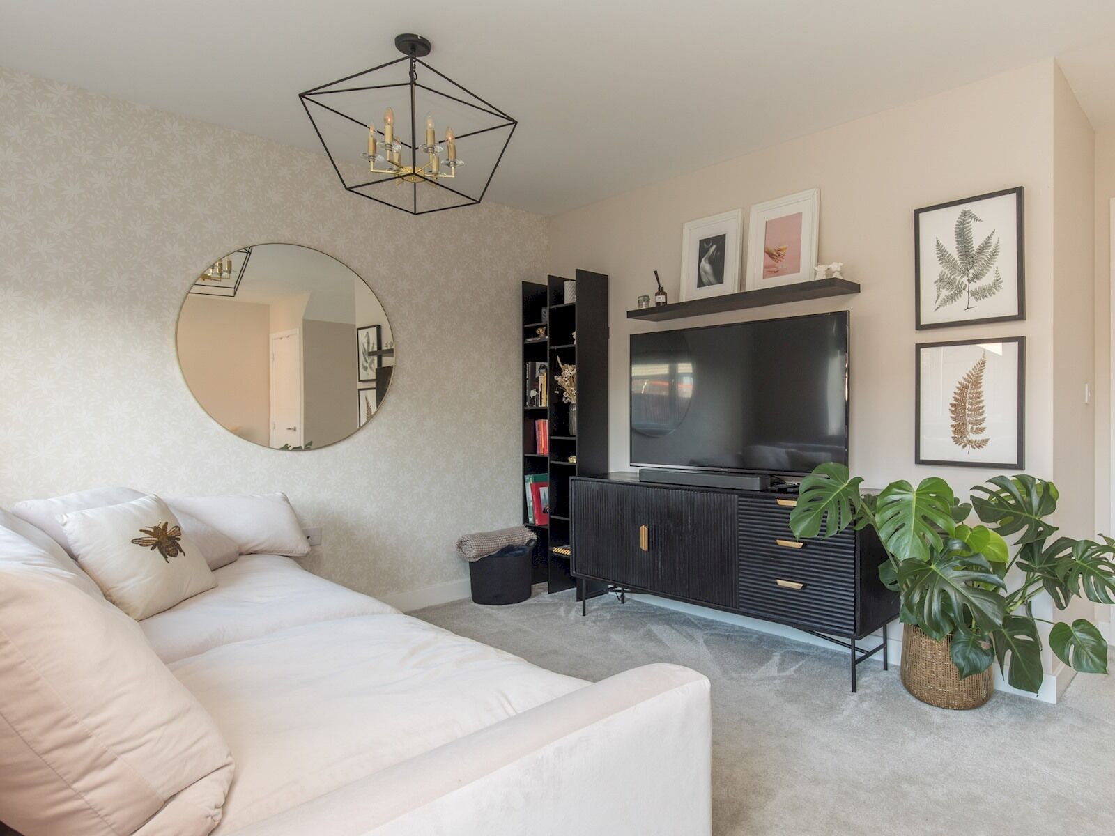 A modern living room with a sofa, a round mirror, a black entertainment unit, and a large flat-screen TV.
