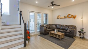A modern living room with a sectional sofa, a coffee table, a ceiling fan, and a staircase. - ​🎉Celebrate in Style! Game Room, 🎱Pool Table,  💃🏼 Dance Pole! (Nashville)