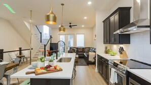 A modern kitchen with a central island, stainless steel appliances, and a dining area with a view of the living room. - ​🎉Celebrate in Style! Game Room, 🎱Pool Table,  💃🏼 Dance Pole! (Nashville)