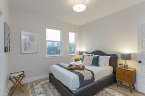 A bedroom with a large bed, bedside tables, a small table with books, and a door. - ​🎉Celebrate in Style! Game Room, 🎱Pool Table,  💃🏼 Dance Pole! (Nashville)