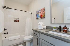 A modern bathroom with a bathtub, toilet, and shower. There are toiletries on the counter, a towel rack, and a mirror. - ​🎉Celebrate in Style! Game Room, 🎱Pool Table,  💃🏼 Dance Pole! (Nashville)
