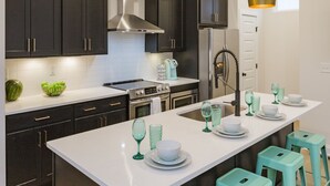 A modern kitchen with dark cabinets, a white island, and teal bar stools. - ​🎉Celebrate in Style! Game Room, 🎱Pool Table,  💃🏼 Dance Pole! (Nashville)