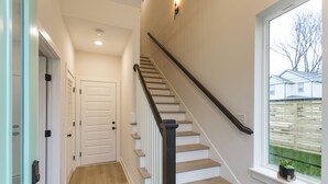 A staircase with wooden steps and a black handrail, leading to a landing with a white door and a small potted plant on the windowsill. - ​🎉Celebrate in Style! Game Room, 🎱Pool Table,  💃🏼 Dance Pole! (Nashville)