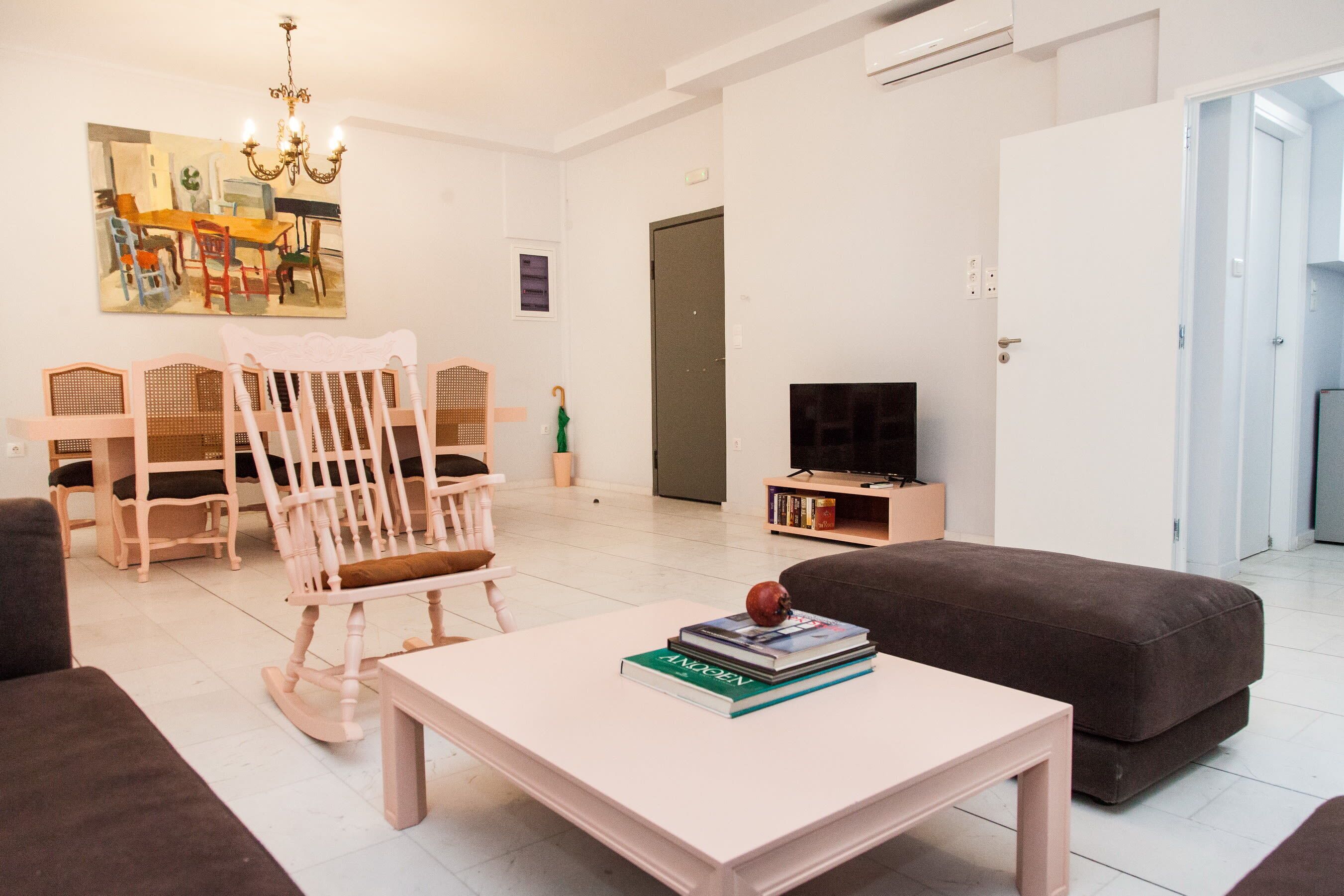 A modern living room with a white coffee table, a brown sofa, a rocking chair, and a television on a stand.