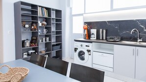 A modern kitchen with a built-in washer and dryer, a coffee maker, and a bookshelf filled with books and kitchenware. - Luxury maisonette in Ilioupoli (Ilioupoli)