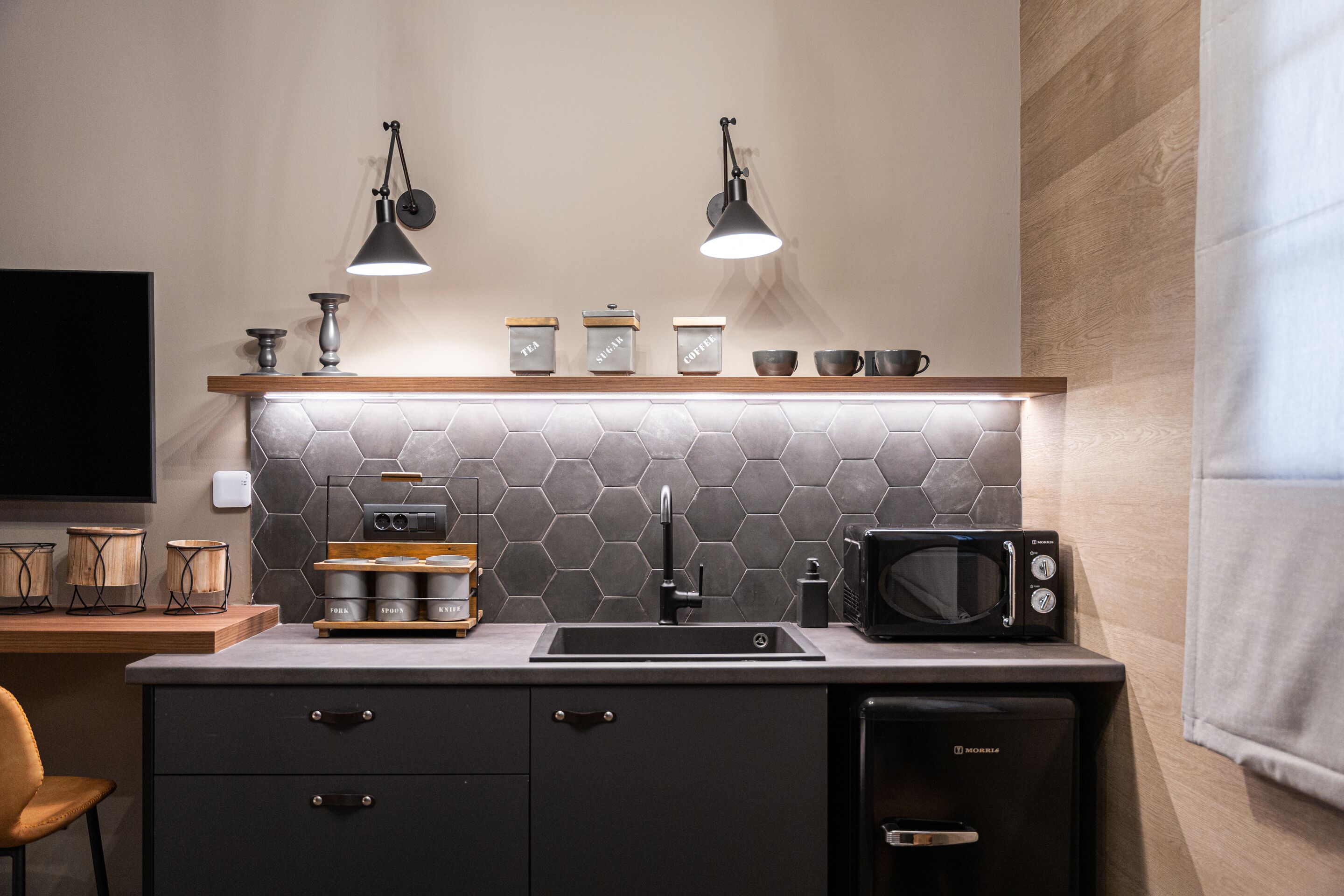Una cocina moderna con encimera negra, microondas, fregadero y dos lámparas colgantes.