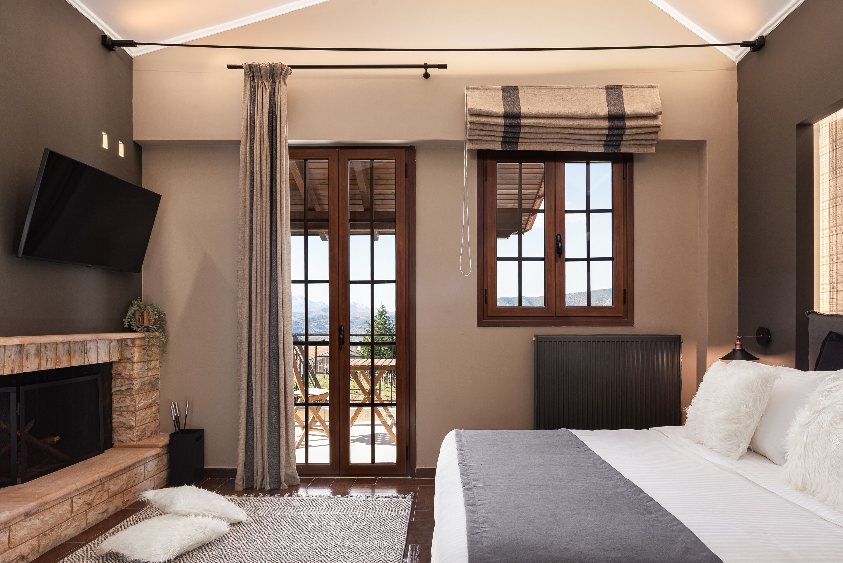 A bedroom with a fireplace, a bed, a window with curtains, and a view of the outdoors.