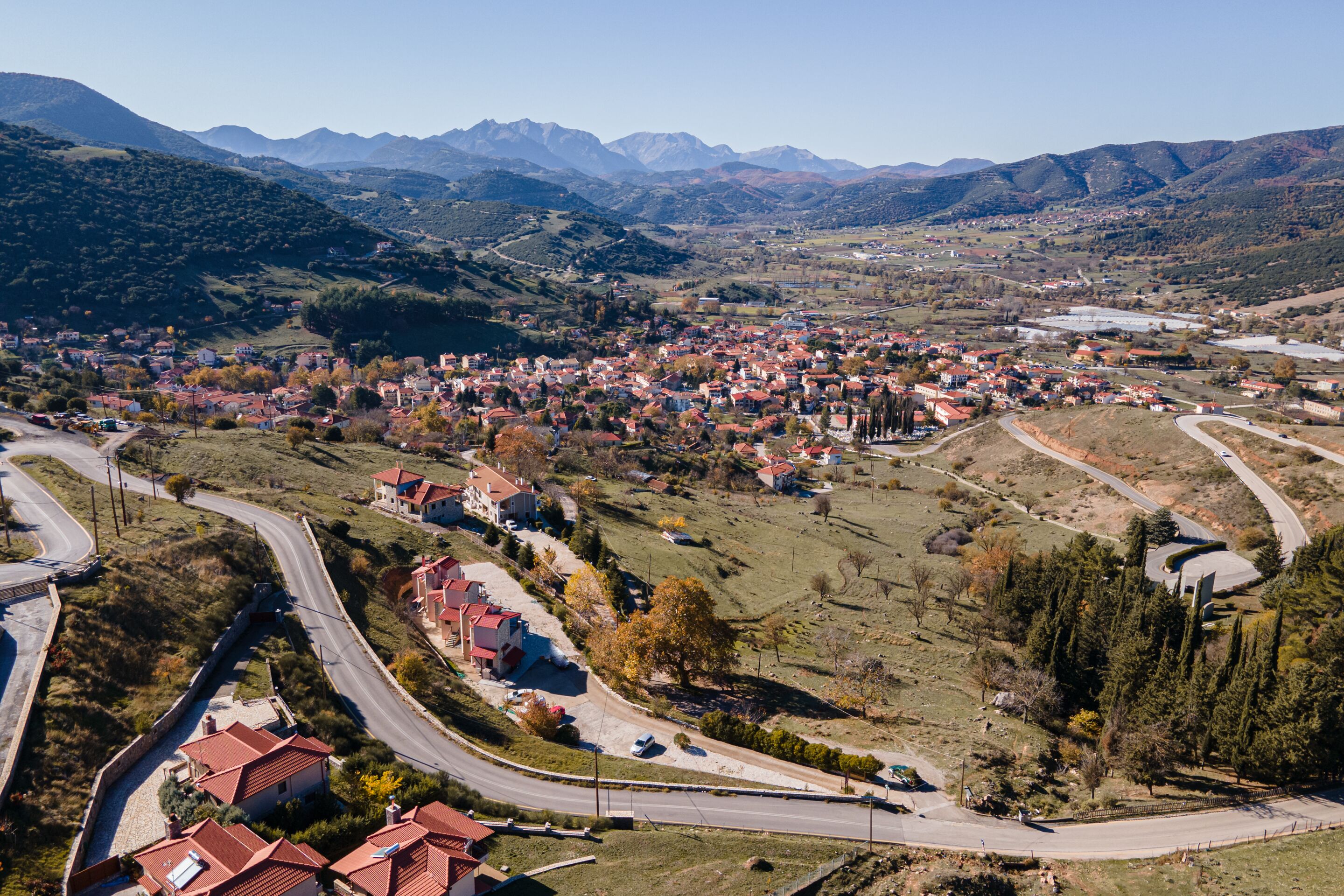 A town nestled in a valley with a winding road and houses with red roofs.