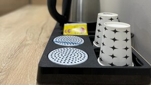 Una bandeja negra con un hervidor, una tarjeta amarilla y dos tazas estampadas.