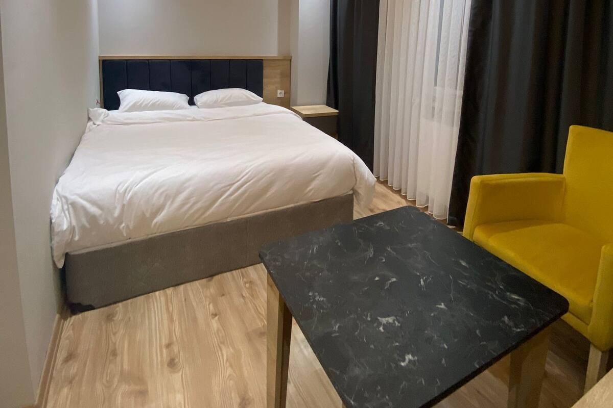 A modern hotel room with a large bed, a small table, and a yellow chair.