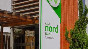 A sign for Hotel Nord EASY in Cambinha, featuring a modern building with a sloped roof and a brick facade.