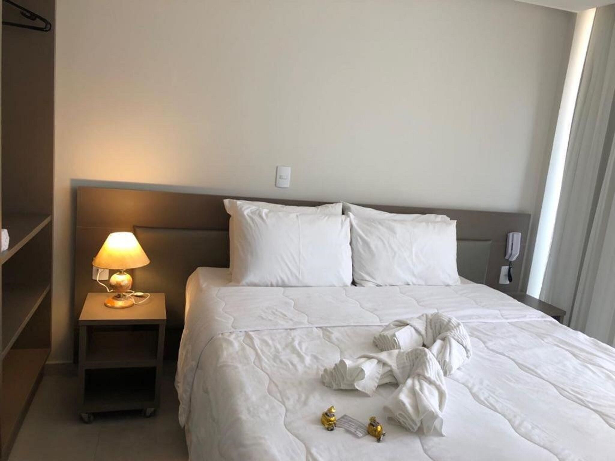 Een hotelkamer met een net opgemaakt bed, een bedlampje, een telefoon en een plankje.