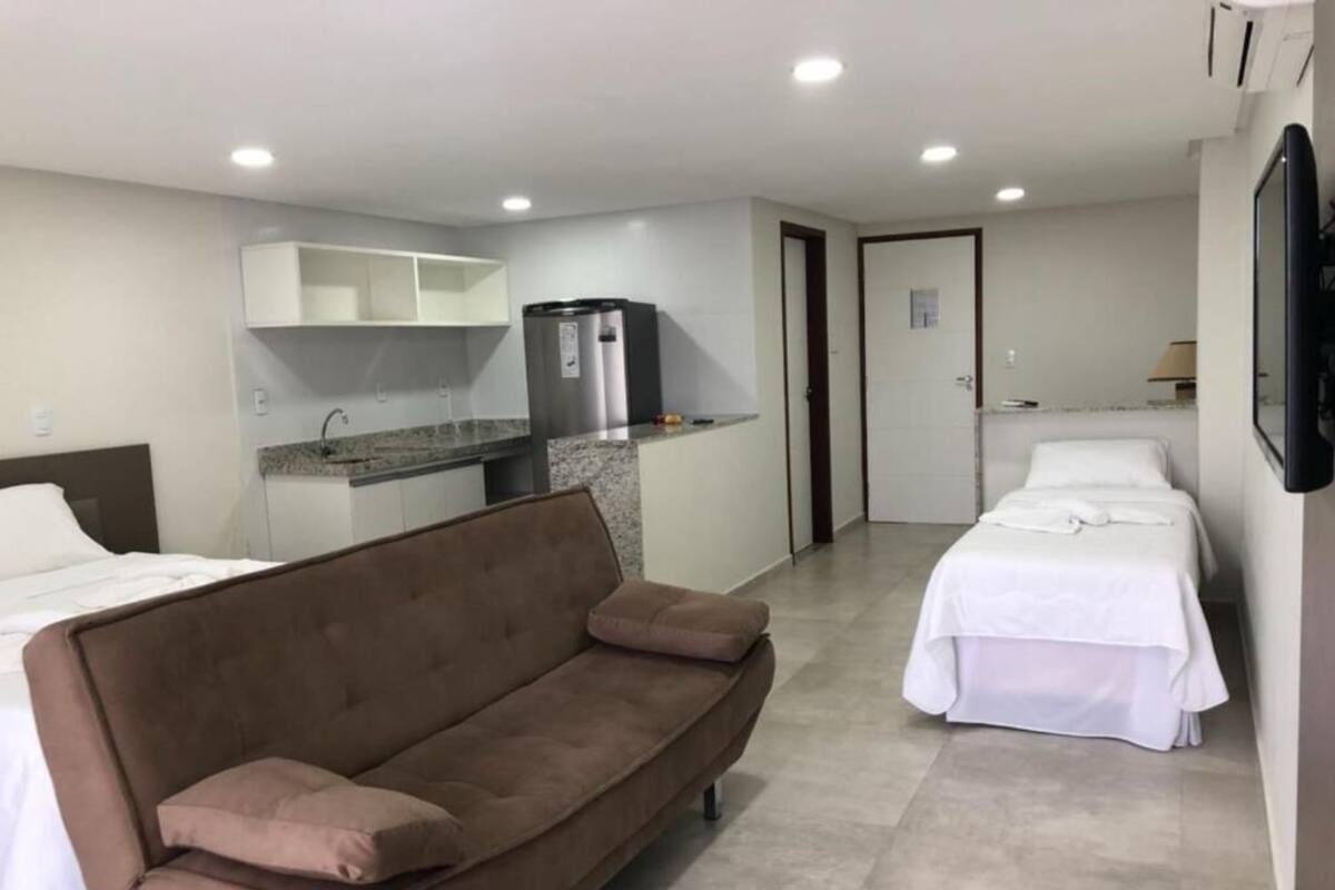 A hotel room with a kitchenette, a sofa, two beds, and a TV.