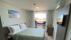 A hotel room with a bed, a small table, a TV, and a window with a view of buildings.