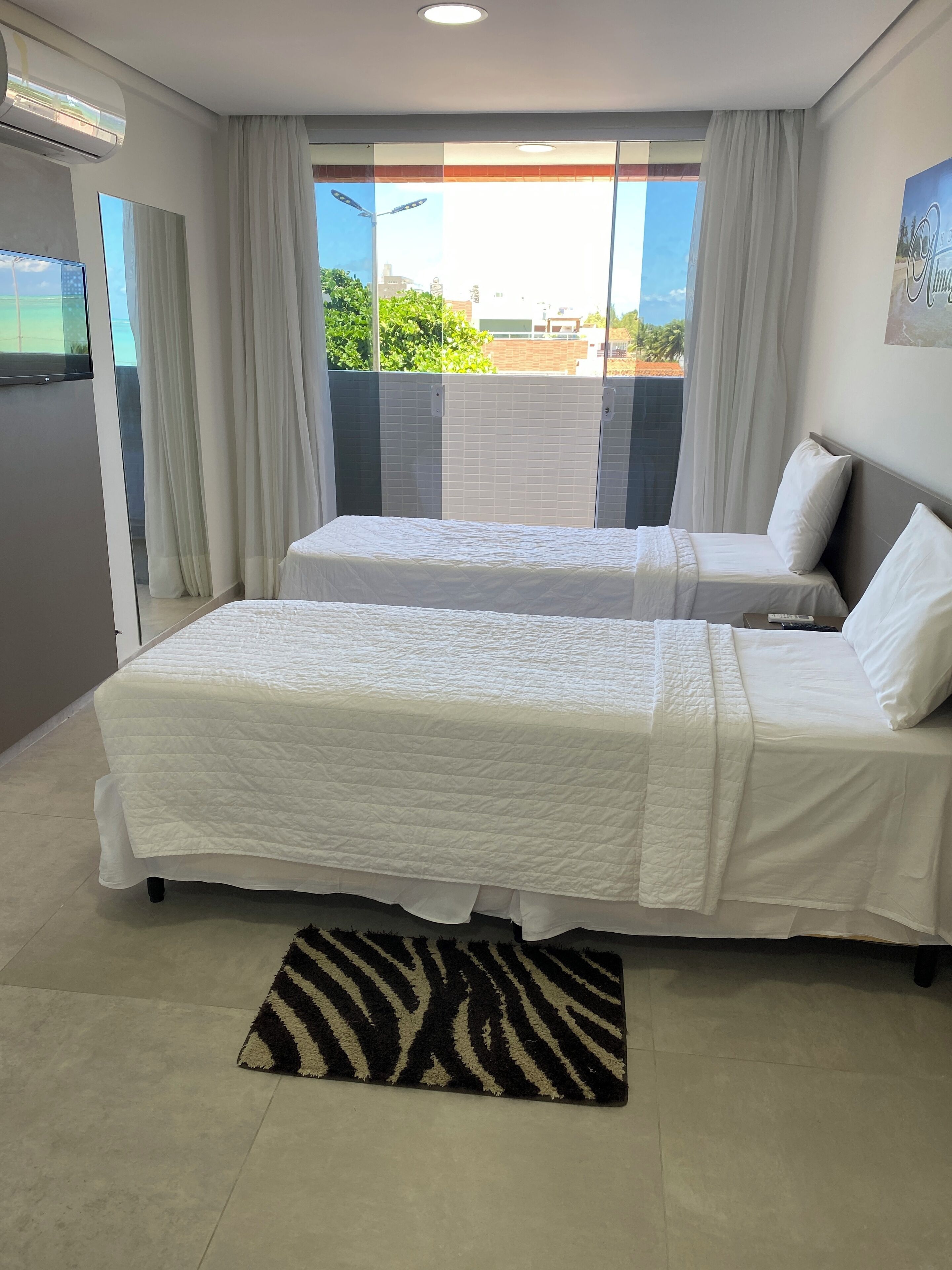 Habitación de hotel con dos camas, un alfombra estampado de cebra y vistas a la ciudad a través de amplias ventanas.