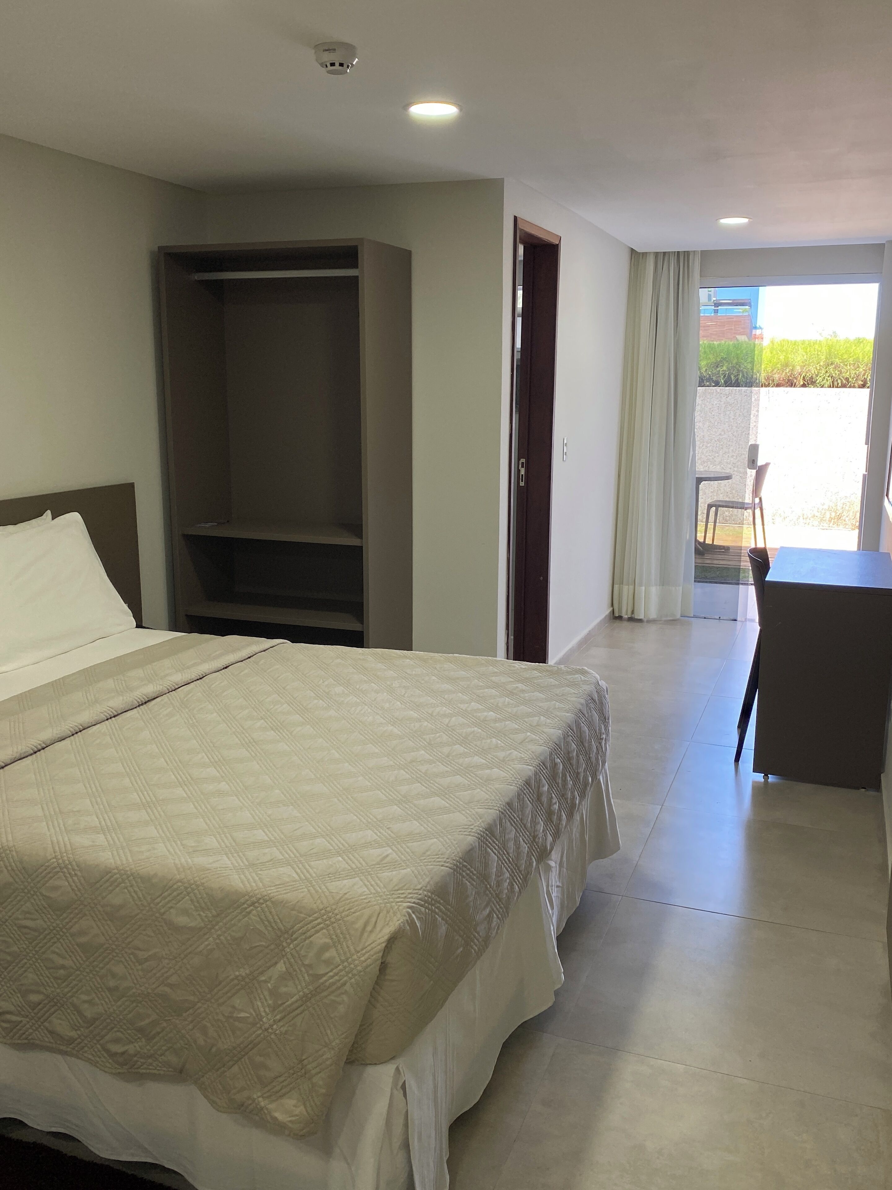 A hotel room with a large bed, a wardrobe, a desk, and a balcony with a view.