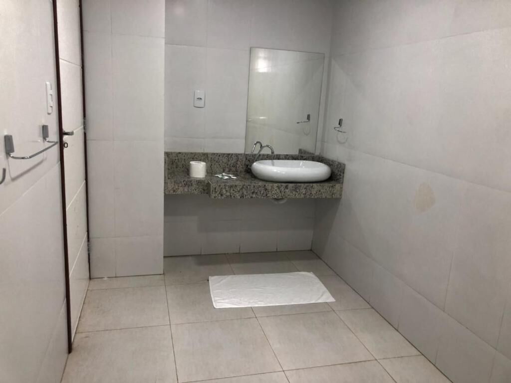 Een kleine, schone badkamer met een witte wastafel, een spiegel en een handdoek op de vloer.