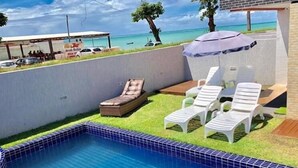 A swimming pool with lounge chairs and a small deck area, overlooking a beach.