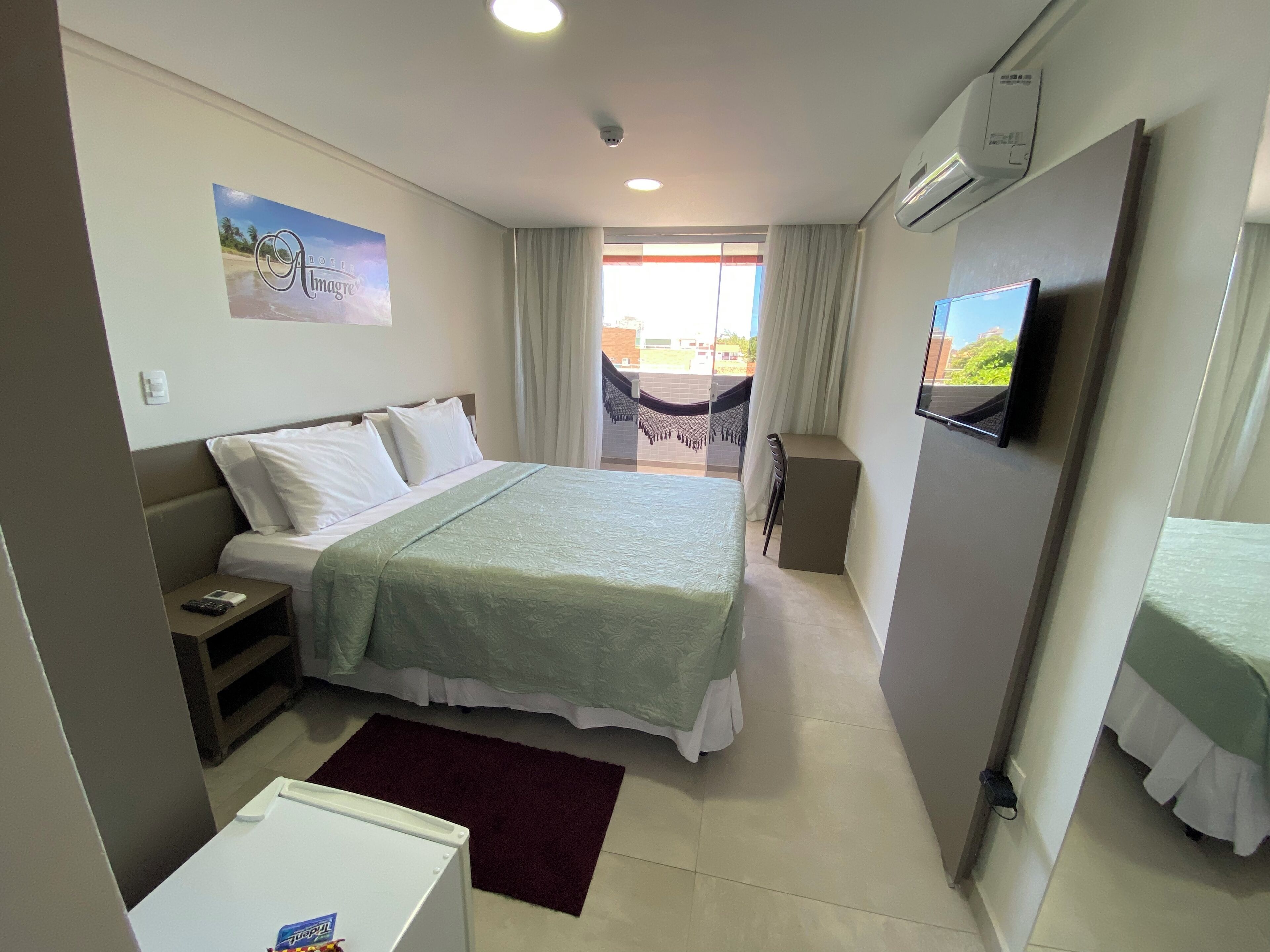 Habitación de hotel con cama, escritorio, silla, televisor y balcón con vistas.