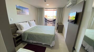 Habitación de hotel con cama, escritorio, silla, televisor y balcón con vistas.