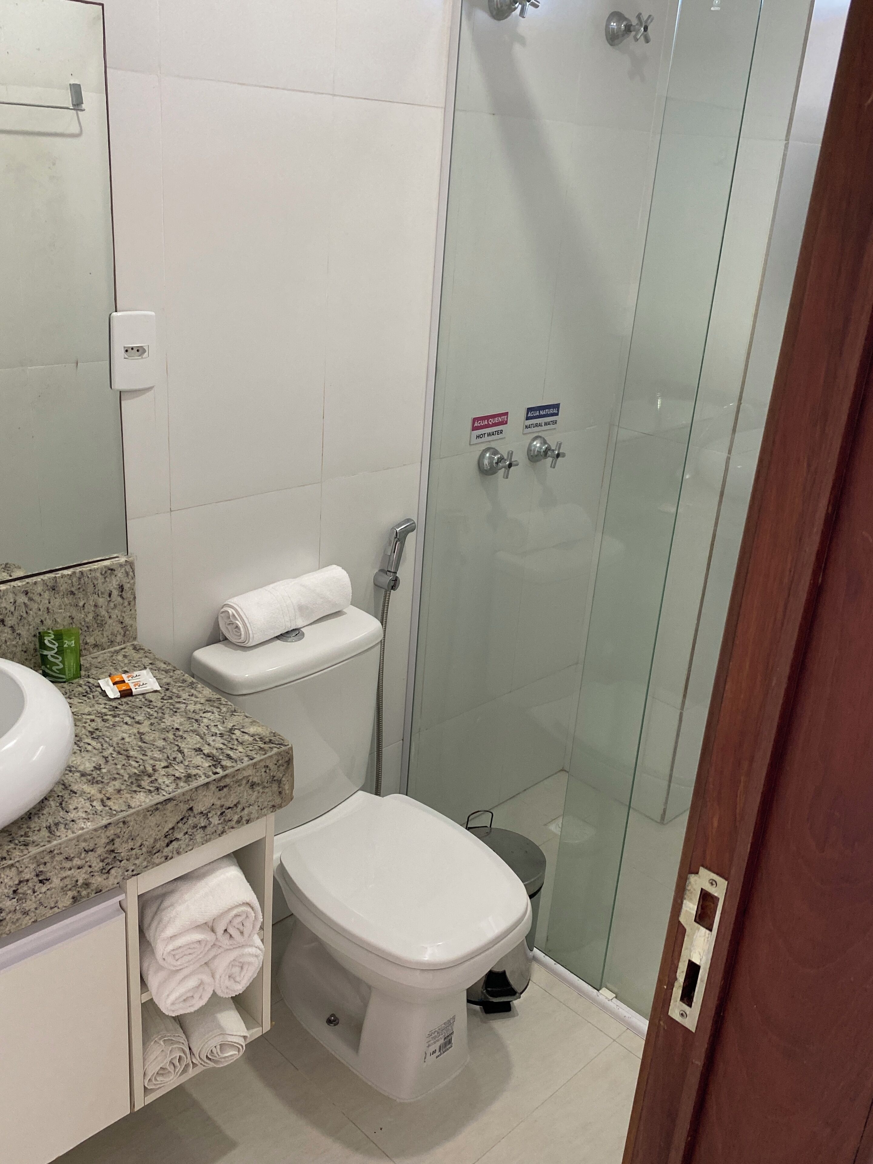 Une salle de bain dotée d’un comptoir en granit, de toilettes, d’une douche à parois de verre et d’un porte-serviettes.
