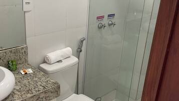 Une salle de bain dotée d’un comptoir en granit, de toilettes, d’une douche à parois de verre et d’un porte-serviettes.