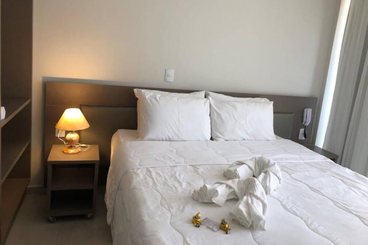 A neatly made bed with white linens, a bedside lamp, and a small nightstand.
