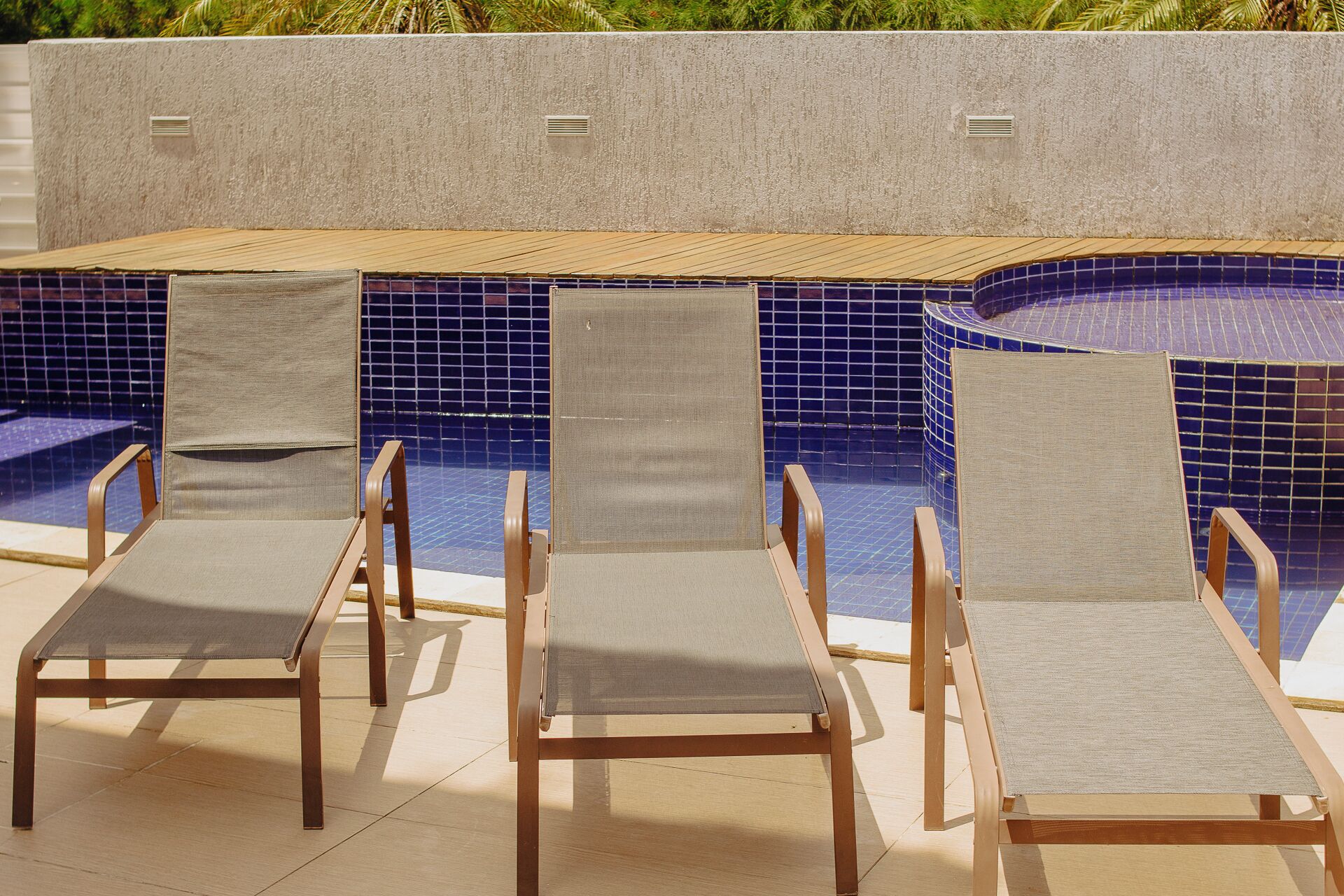 Un área junto a la piscina con tres sillas reclinables y una piscina con azulejos.