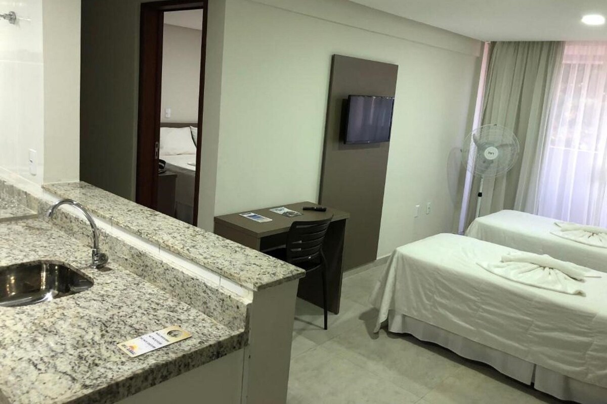 Une chambre d’hôtel équipée d’un lavabo avec un plan de travail en granit, d’un bureau, d’un lit, d’un téléviseur fixé au mur et d’un ventilateur sur pied.