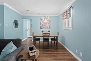 A dining area with a wooden table and chairs, a chandelier, and a wall clock.