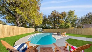 Ein Garten mit Pool, Holzterrasse und Liegestühlen.