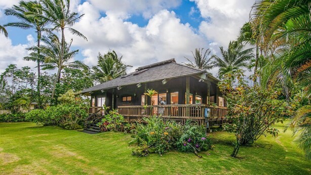 Una casa de madera con porche, rodeada de exuberante vegetación y palmeras.