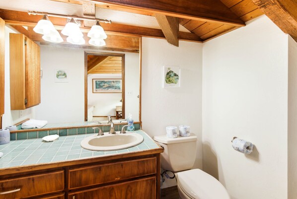A bathroom with a wooden vanity, a sink, a mirror, and a toilet.