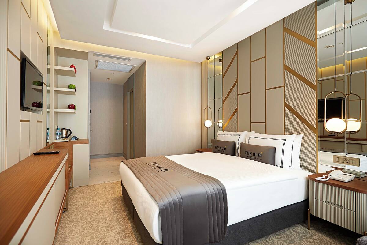 A hotel room with a bed, bedside table, TV, and a mirror.