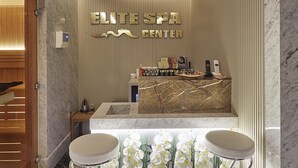 A modern spa center with a reception desk, two bar stools, and a decorative orchid arrangement. - The Hubi Hotel (Istanbul)