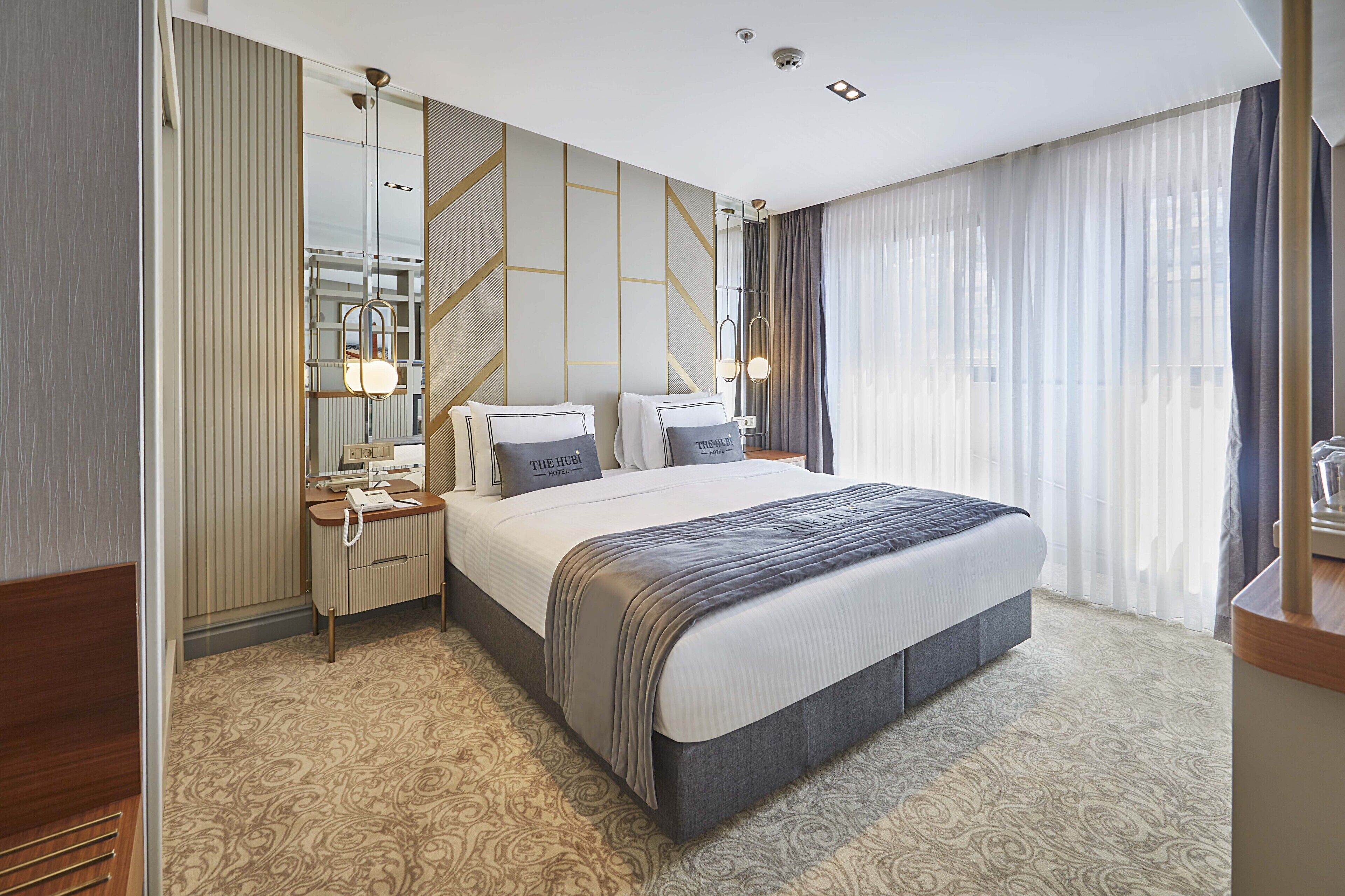 A modern hotel room with a large bed, bedside tables, a mirror, and a wardrobe.
