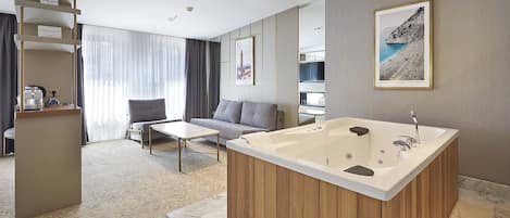 Habitación de hotel moderna con una bañera grande, un sofá, una mesa de centro y vista al mar.