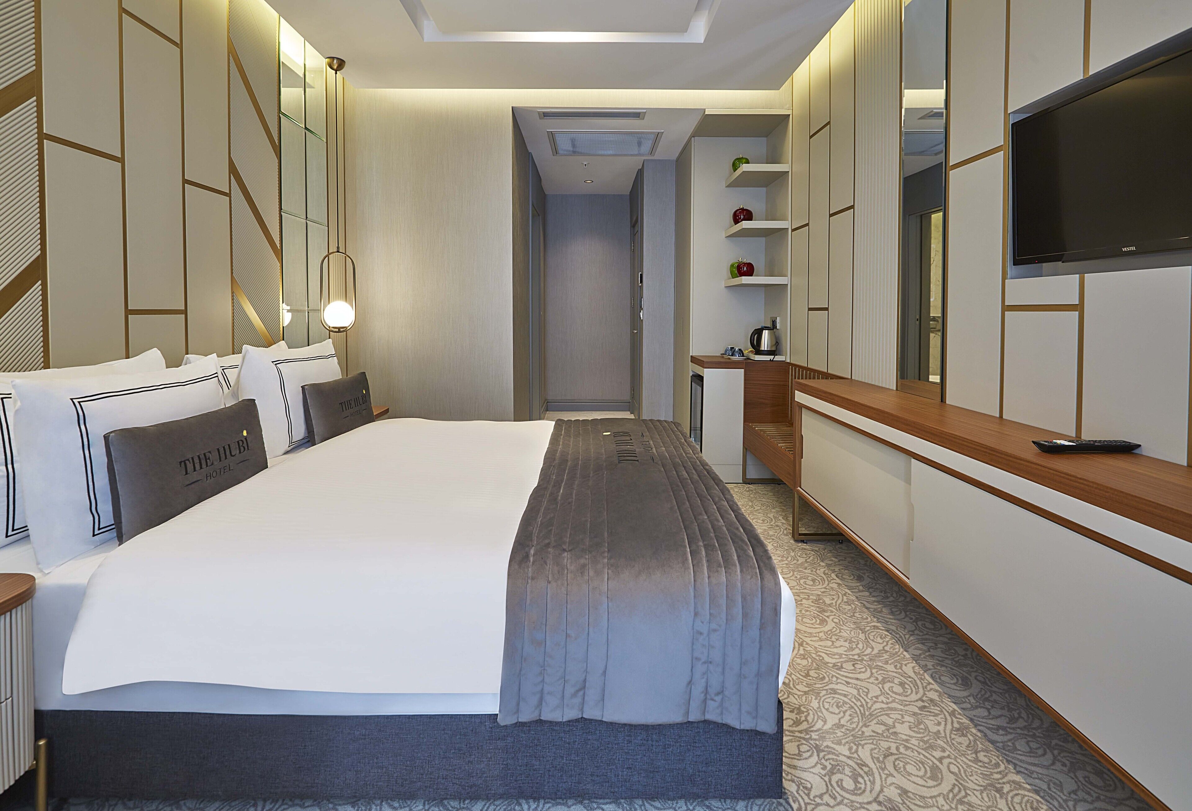 A hotel room with a large bed, a TV mounted on the wall, a desk with a chair, and a wardrobe.