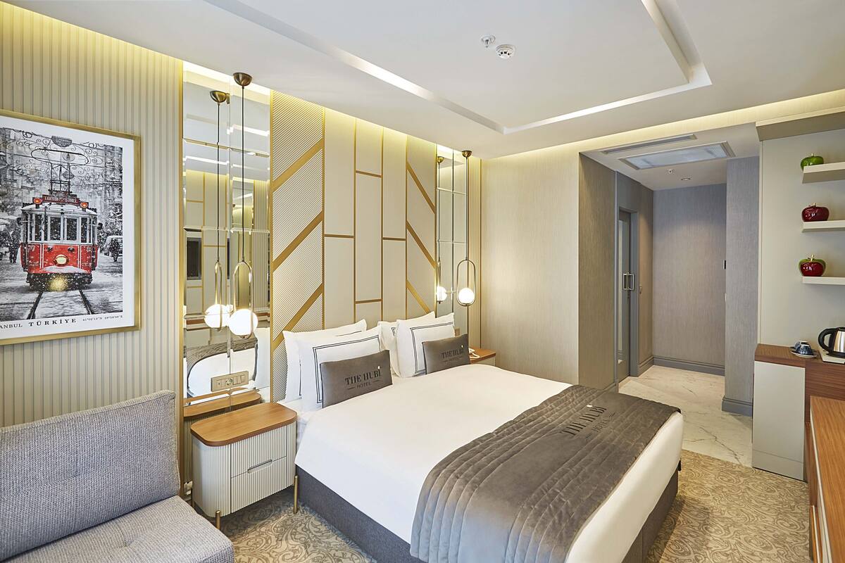 A modern hotel room with a large bed, a sofa, a desk, and a bathroom.