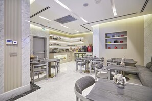 Un hall d’hôtel moderne avec un sol en marbre, des coins salon, une cuisine et un mur avec des étagères.