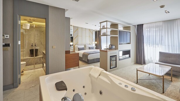 A modern hotel room with a large bathtub, a sofa, a TV, and a shower area. - The Hubi Hotel (Istanbul)