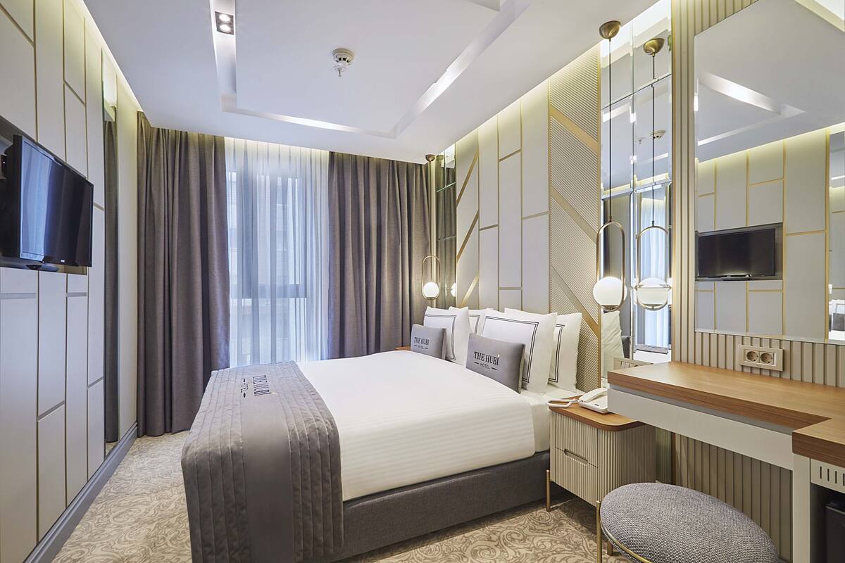 A modern hotel room with a large bed, a desk, a chair, a TV, and a mirror.